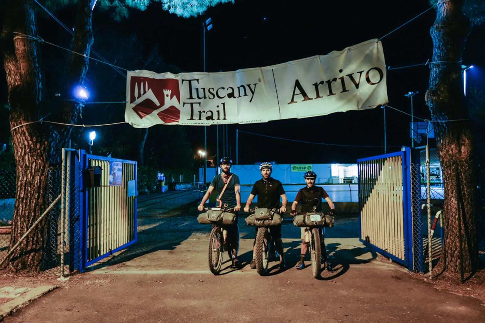 Tre rider sotto l'arco dell'arrivo, di notte